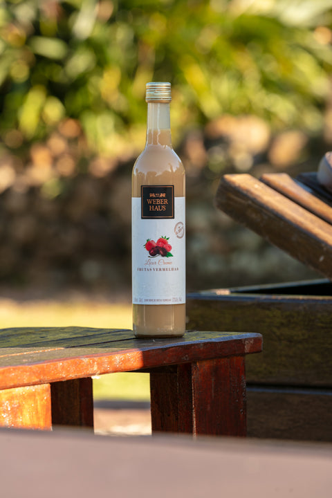 Garrafa de Licor creme Weber Haus Frutas Vermelhas em ambiente externo sobre mesa de madeira.