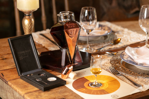 Garrafa de Cachaça Extra Premium Diamant 21 Anos Weber Haus edição limitada, acompanhada de sua roda sensorial e uma taça com uma pequena porção da bebida para degustação.