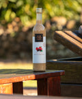 Garrafa de Licor creme Weber Haus Frutas Vermelhas em ambiente externo sobre mesa de madeira.
