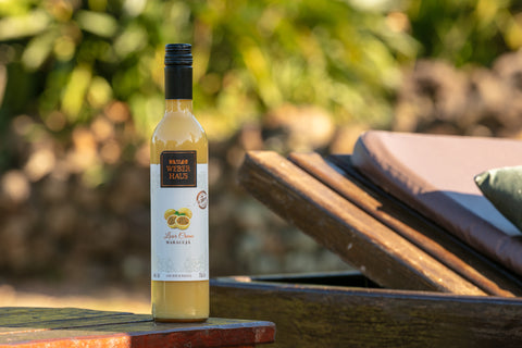 Garrafa de Licor Creme Weber Haus Maracujá em ambiente externo sobre mesa de madeira.