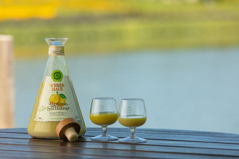 Licor Creme Weber Haus de Limão Siciliano com duas taças pequenas de bojo aberto em ambiente externo sobre mesa de madeira.