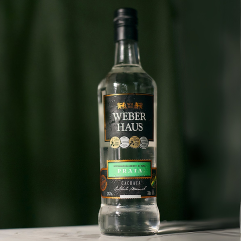 Cachaça Prata Weber Haus em cima de uma mesa e fundo verde